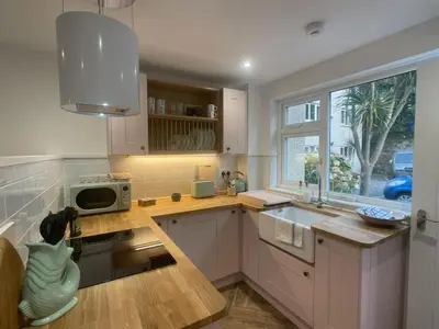 a kitchen with white cabinets and a sink and a window at Beachy Maisonette- 2 Min walk to Porth Beach in Newquay