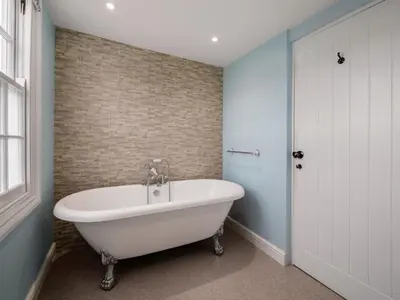 a white bath tub in a bathroom with a brick wall at Holiday Home Cherry Orchards by Interhome in Mevagissey