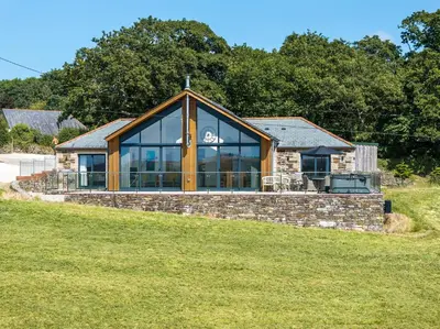 a stone house with large windows on a grass field at Callestock Vean in Truro