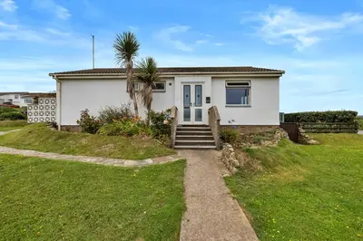 a white house with a palm tree in a yard at Finest Retreats - Sea Thrift at Widemouth Bay in Widemouth Bay