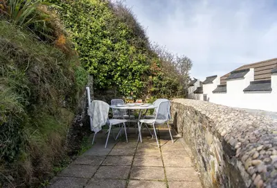 a table and chairs sitting next to a stone wall at The Gatehouse Apartment in Portreath