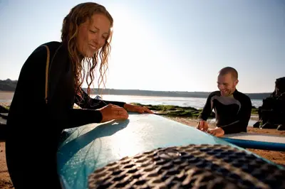 two surfers sitting on the beach with their surfboards at Skydeck at The Liner – Stylish 2-Bed / 2-Bath Top Floor with Panoramic Sea Views in Falmouth