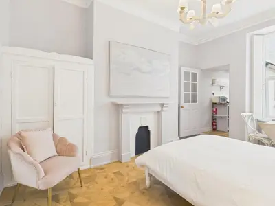a white bedroom with a bed and a chair at Cosy Coastal Falmouth Studio with Free parking & WiFi in Falmouth