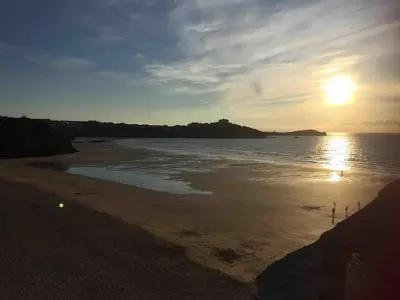 a beach with the sun rising over the ocean at Tolcarne Reach in Newquay