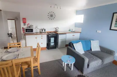 a living room with a couch and a table and a kitchen at Utopia Apartments in Perranporth