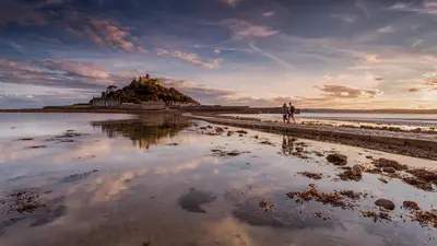 two people walking on the beach with a castle in the background at Jowders Cottage in Marazion