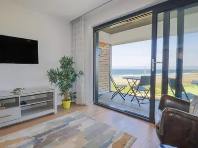 a living room with a television and a balcony with the ocean at Beach View Fistral in Newquay