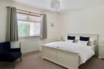 a bedroom with a white bed and a blue chair at Sleeps 9- KingBeds- FamilyFriendly- ContactlessCI in Wadebridge