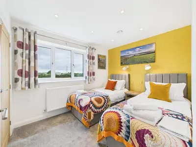 two beds in a room with yellow walls and windows at Roughtor View in Camelford