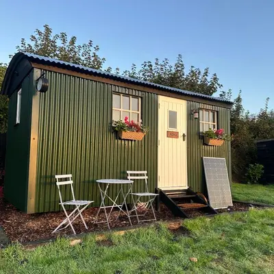 a green shed with two chairs and a table and two windows at Harpers Huts in Lanivet