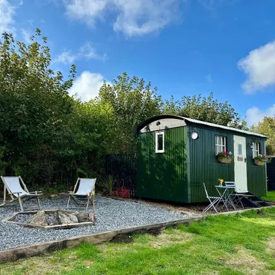 a green tiny house with two chairs on gravel at Harpers Huts in Lanivet