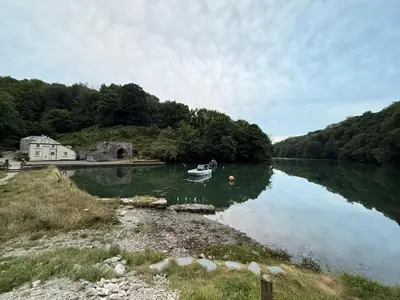 a boat in a lake with a house and trees at Finest Retreats - Three Quarter Cottage in Bodinnick