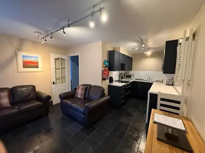 a living room with two leather chairs and a kitchen at Hollowell House Holiday Apartment in Boscastle