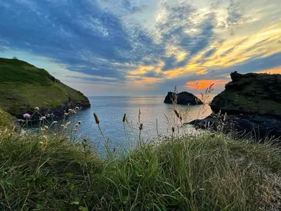 a sunset over a body of water with rocks at Hollowell House Holiday Apartment in Boscastle