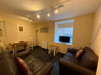 a living room with a leather couch and a table at Hollowell House Holiday Apartment in Boscastle