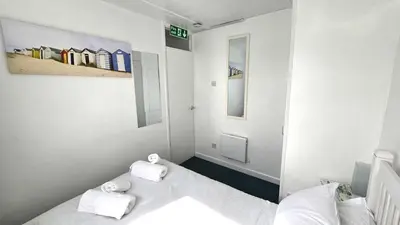 a small white room with two beds and towels at Chalet 150, Perran Sands in Perranporth