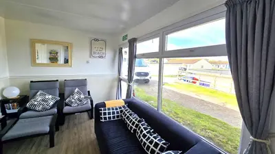 a living room with a couch and a large window at Chalet 150, Perran Sands in Perranporth