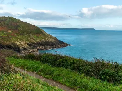 a path on a hill next to the ocean at Holiday Home Mermaid Cottage by Interhome in Mevagissey