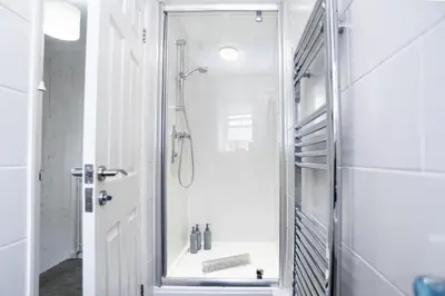 a white bathroom with a shower with a glass door at St Ives Holiday Cottage with Parking – Coastal Retreat in St Ives