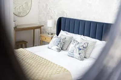 a bed with a blue headboard and pillows on it at St Ives Holiday Cottage with Parking – Coastal Retreat in St Ives