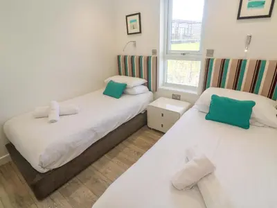 two beds in a small room with green and white pillows at Lodge 83, Gwel an Mor in Redruth