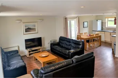 a living room with black leather furniture and a kitchen at Atlantic Lodge - 4 Bedroom - Pool -Spa - Gym in Newquay