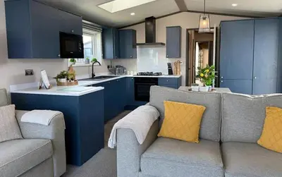 a living room with a couch and a kitchen with blue cabinets at Vyvyenne Lodge in Padstow