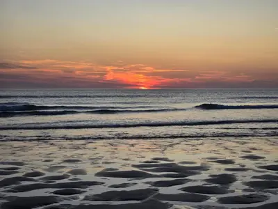 a sunset on a beach with the ocean at Lowenek House in Perranporth