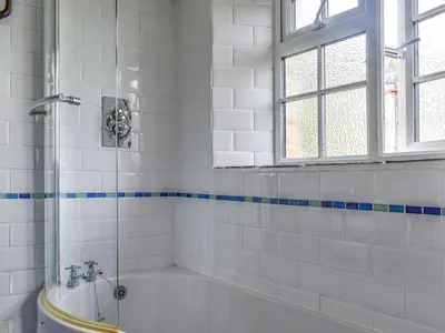 a white tiled bathroom with a tub and a window at Nutmeg's - Uk50373 in Camelford