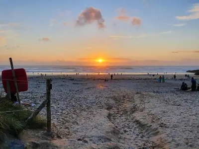 a sunset on a beach with people and the ocean at Towan Valley, Porthtowan - Coastal 3 Bedroom Eco-Home with Hot Tub in Truro