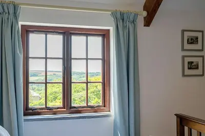 a window with blue curtains in a bedroom at Finest Retreats - Demelza Cottage in Blisland