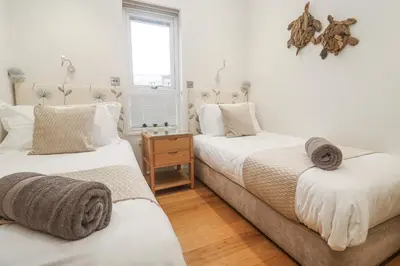two beds in a bedroom with white walls and wooden floors at The Black Barnacle in Redruth