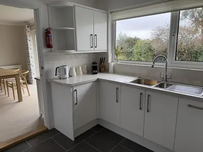 a kitchen with white cabinets and a sink and a window at 42 Little Trelyn in Wadebridge