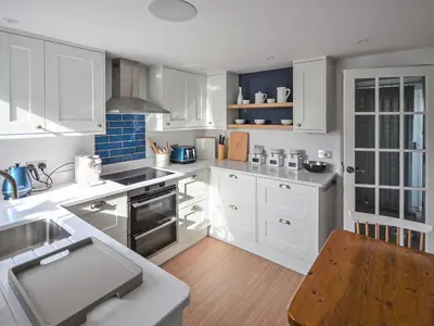 a kitchen with white cabinets and a wooden table at Fuchsia Cottage in Saint Mawes