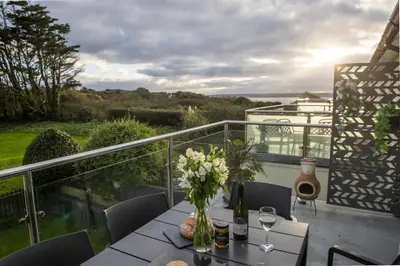 a table with a vase of flowers on a balcony at Sunset View - Sea View - Pet Friendly - Free WiFi - Free Parking in Marazion