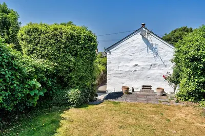 a small white building with a bench in a yard at Finest Retreats - Forge Cottage, Padstow in Padstow