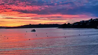 a boat in a body of water with a sunset at The Red House Annexe in Saint Mawes