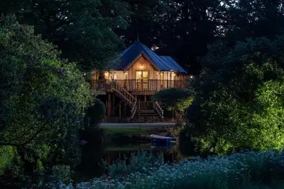 a large wooden cabin with a deck and a pond at Landal Clowance in Crowan