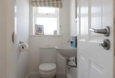 a white bathroom with a toilet and a sink at Little Tresevens in Polzeath