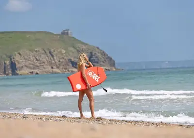 a woman walking on the beach with a surfboard at Praa Sands Holiday Park in Praa Sands