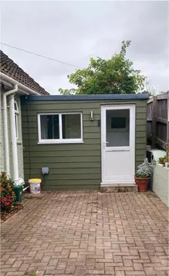 a green house with a white door and a brick driveway at Chy An Geddon in Penryn