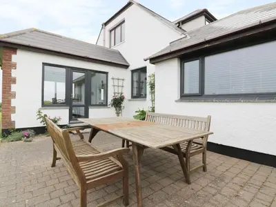 a wooden table and two chairs in front of a house at Chynoweth in Crantock