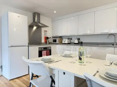 a kitchen with white cabinets and a table with wine glasses at Pennys Place in St Ives