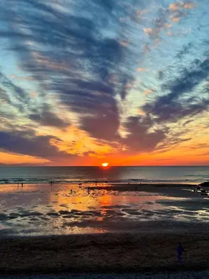a sunset at the beach with people walking on the beach at Boho Bali-style Beach House near Fistral in Newquay