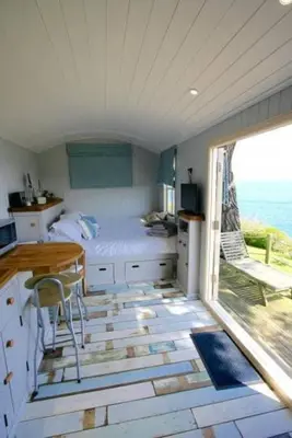 a bedroom with a bed and a table and a window at Shepherd's Hut Gorran Haven Panoramic Ocean Views in Gorran Haven