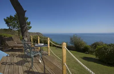 a table and chairs on a wooden deck with the ocean at Shepherd's Hut Gorran Haven Panoramic Ocean Views in Gorran Haven
