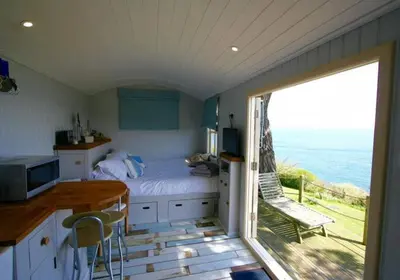 a bedroom with a bed and a view of the ocean at Shepherd's Hut Gorran Haven Panoramic Ocean Views in Gorran Haven