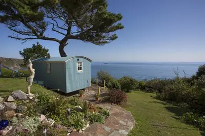a tiny house in a garden with a tree at Shepherd's Hut Gorran Haven Panoramic Ocean Views in Gorran Haven