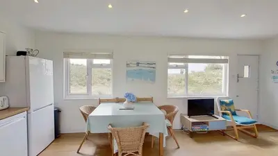 a kitchen with a white table and chairs and a refrigerator at G24 Trelinda, Riviere Towans in Hayle