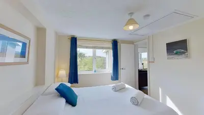 a bedroom with a white bed with blue pillows and a window at G22 Happy Days, Riviere Towans in Hayle